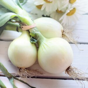 Close-up of fresh spring onions on a rustic white wooden table with daisies.